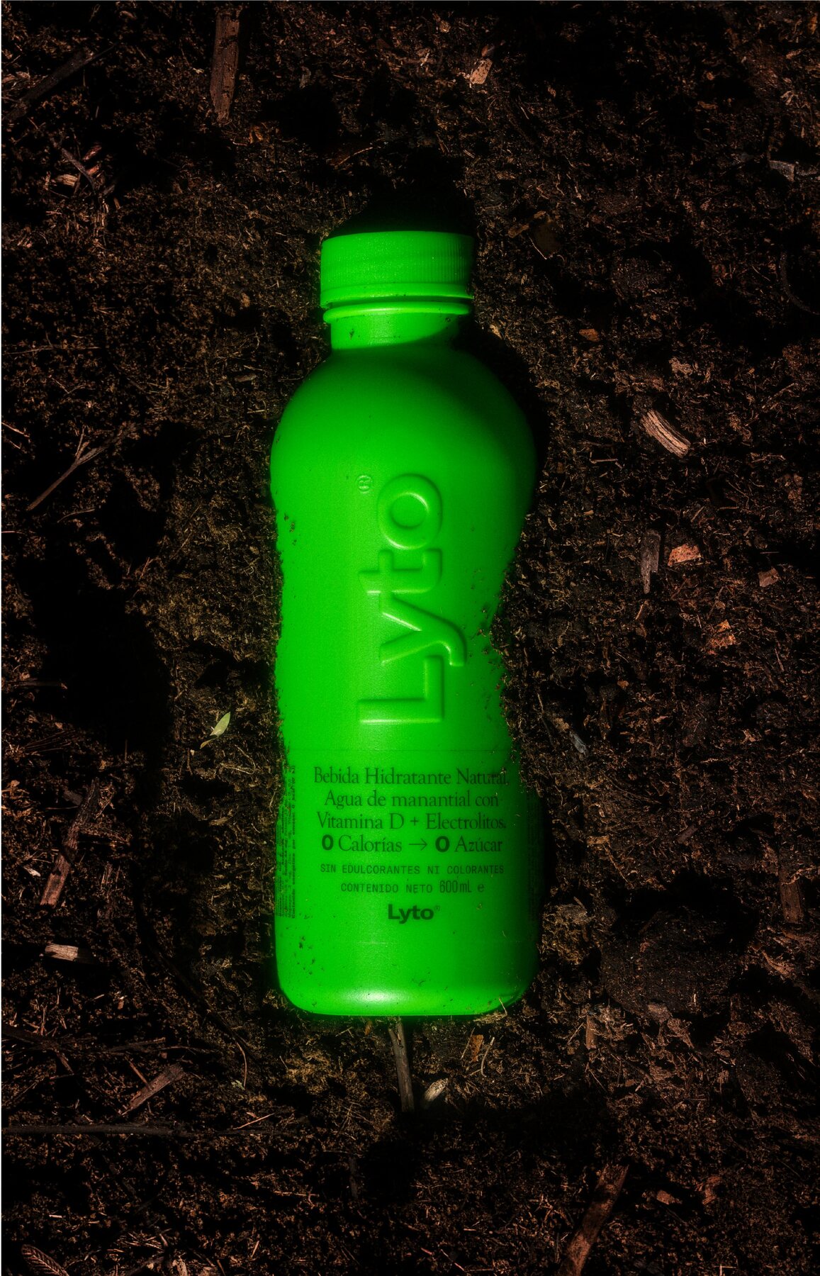 Green Lyto bottle resting on dark soil