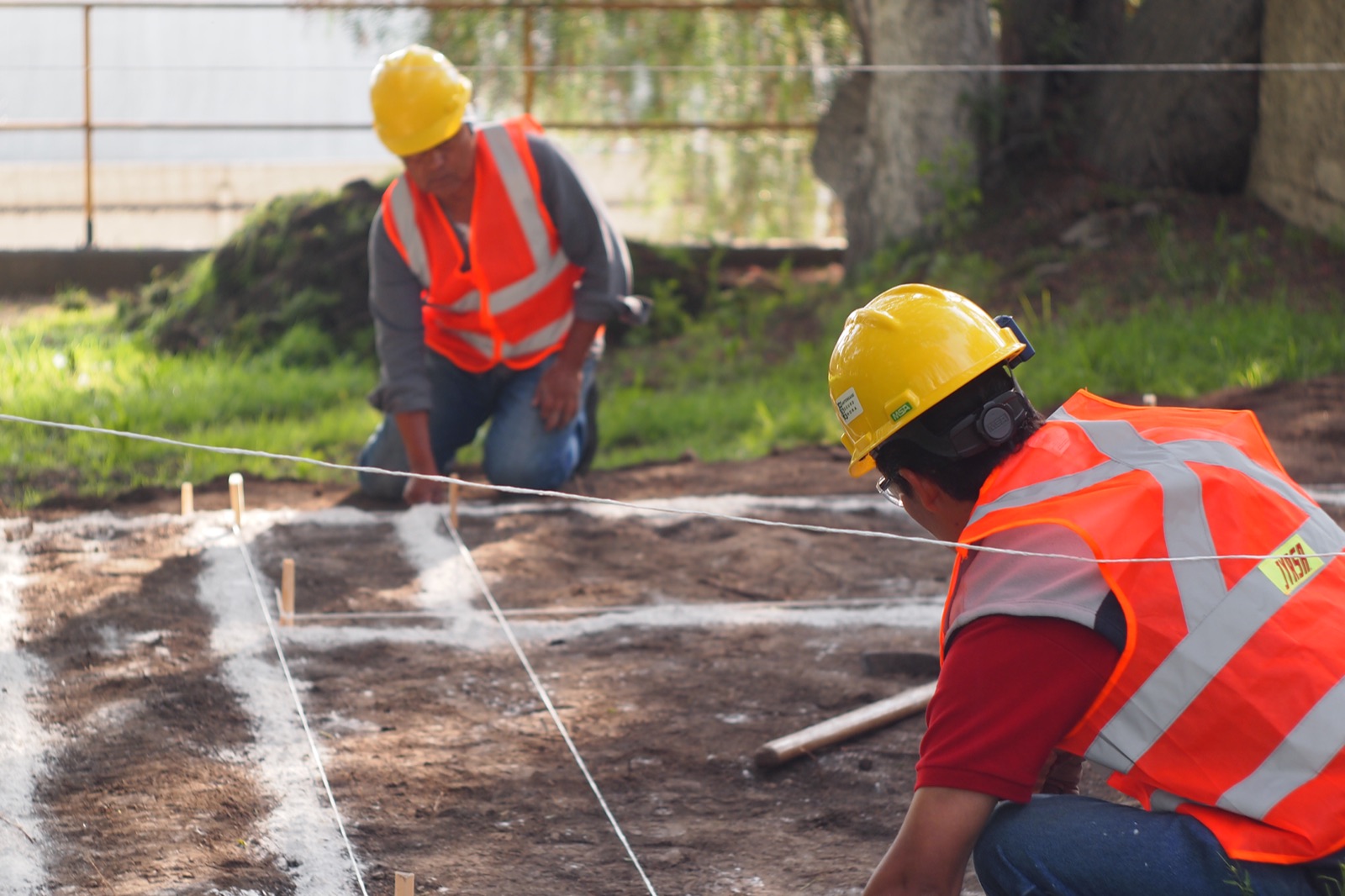 Two workers in hard hats laying out the foundation with string lines